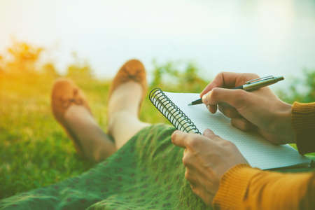 female hands with pen writing on notebook on grass outsideの写真素材