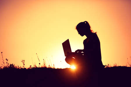 silhouette of a girl with laptop on sunset or sunrise backgroundの写真素材