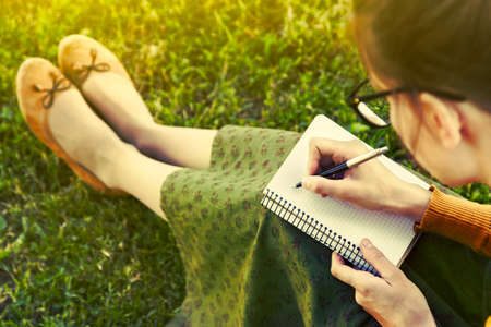 girl with pen writing on notebook on grass outside