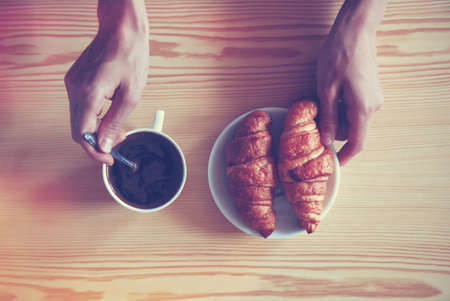 Hands holding cup of coffee and croissants. View from aboveの写真素材
