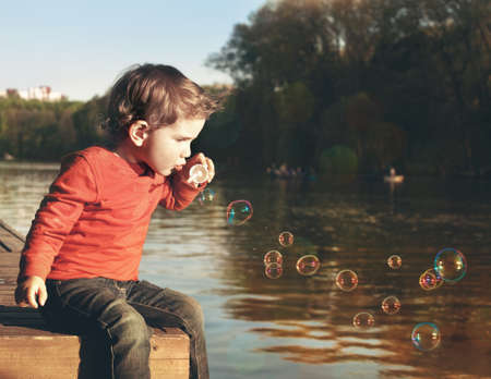 Little boy blowing soap bubbles at a lakeの写真素材