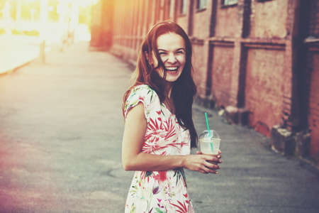 pretty laughing girl with milk shake walking at morning streetの写真素材
