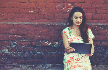 girl holding digital tablet pc near brick wallの写真素材