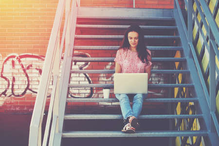 Pretty girl working with laptop sitting on stairs of stairwayの写真素材