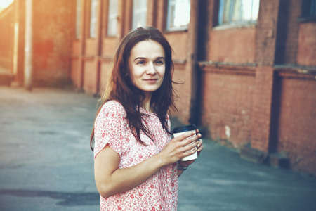 smiling pretty girl walking in street with morning coffeeの写真素材
