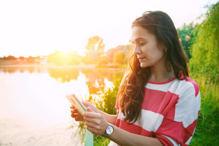 girl holding digital tablet pc at lake shore in summer sunrise lightの写真素材