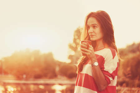 pretty girl with morning coffee at river sunriseの写真素材