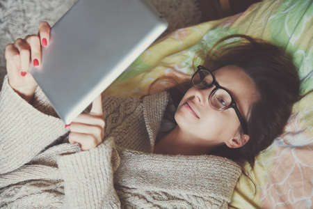 woman lying in bed with digital tablet touching with finger in morningの写真素材