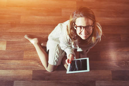 Woman sitting on wooden floor with digital tablet touching with finger. View from aboveの写真素材