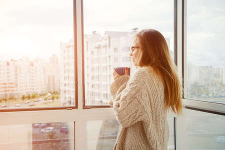 pretty girl drinking coffee or tea in morning sunlight near window