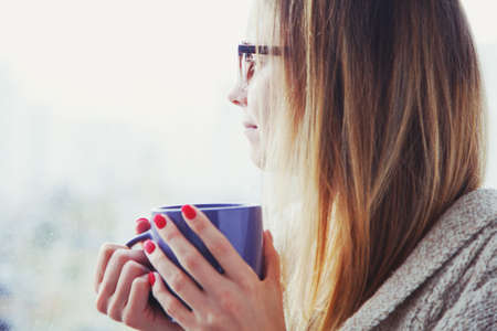 pretty girl drinking coffee or tea in morning sunlight near window