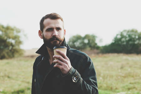 Bearded man with paper cup of morning coffee walking in parkの写真素材