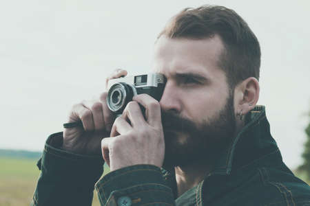 Bearded man holding retro camera and taking photoの写真素材