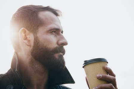 Bearded man with paper cup of morning coffee in sunlightの写真素材