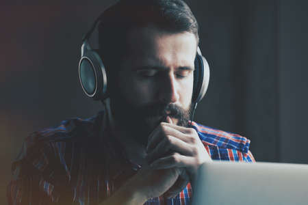 handsome bearded man  in headphones listening to music with laptopの写真素材