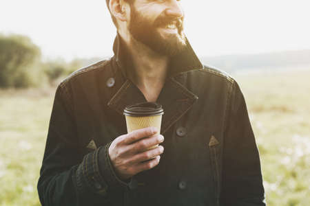 handsome bearded man with paper cup of morning coffee walking in parkの写真素材
