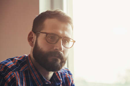 handsome bearded man in checkered shirt and glasses thinking