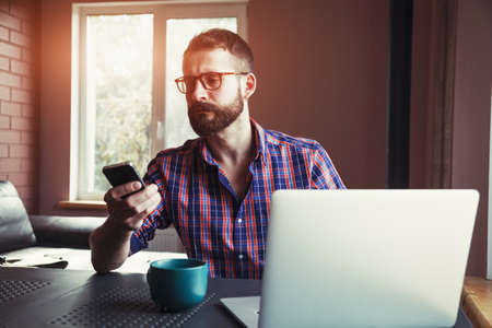 bearded man working with laptop and phone in morning sunlightの写真素材