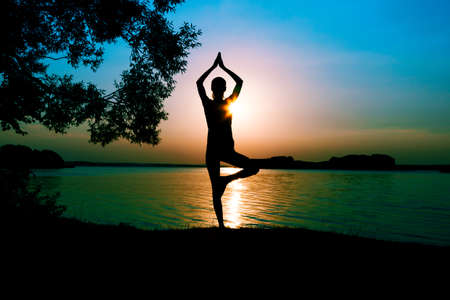 Silhouette woman practicing yoga posing on beach at sunsetの写真素材