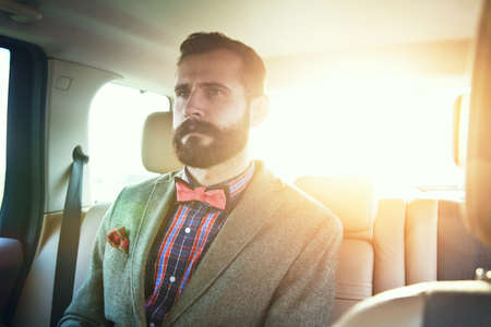 handsome bearded businessman sitting on back seat of carの写真素材