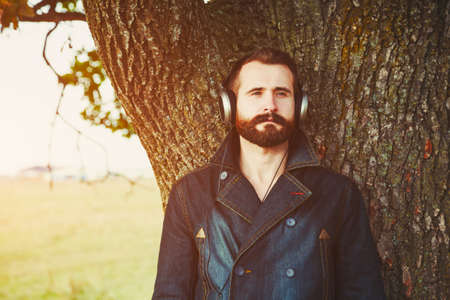 handsome bearded man  in headphones listening to music near natural treeの写真素材
