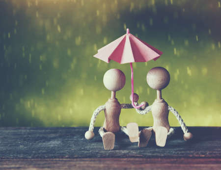 Romantic wooden little men as couple sitting under umbrella in rainの写真素材