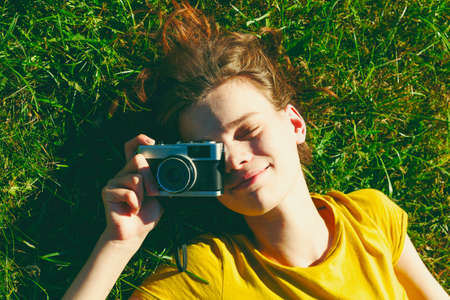 smiling girl lying in grass with film cameraの写真素材