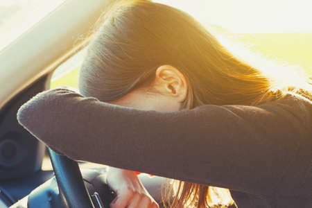 stressed or tired girl in car lying on steering wheel