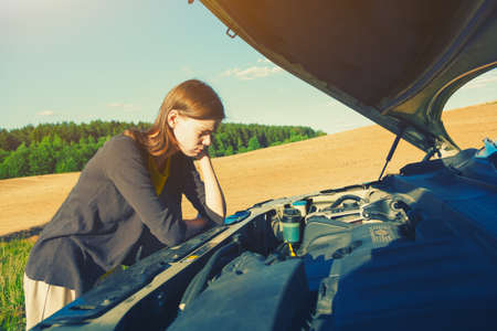 sad girl looking under hood of breakdown car