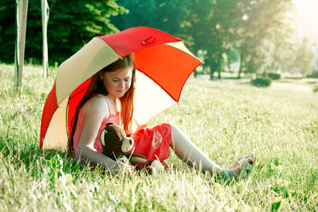 cute redhead girl with teddy bear under summer umbrella. friendship conceptの写真素材