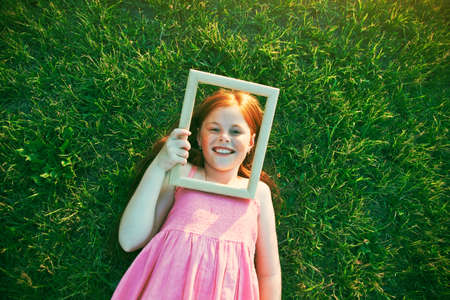 Smiling redhead girl lying in grass with wooden frame as portrait