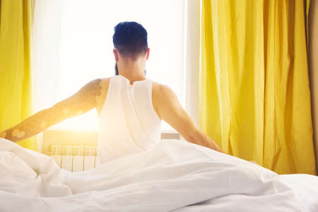Bearded man in bed raising hands facing the sunrise at morningの写真素材
