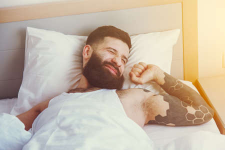 Bearded man in bed raising hands facing the sunrise at morningの写真素材