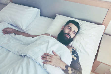 Bearded man lying in bed in morningの写真素材