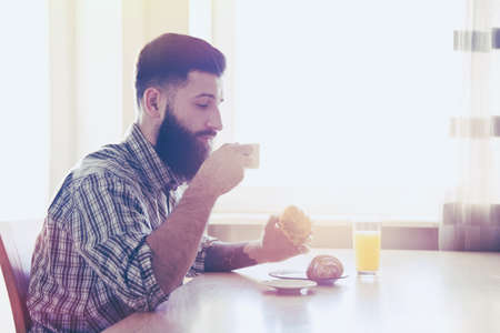 bearded man having breakfast with cup of morning coffee and croissantsの写真素材