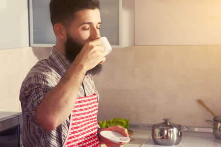 bearded man drinking cup of morning coffee at kitchenの写真素材