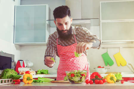 awesome bearded man cooking at kitchen making healthy vegetable saladの写真素材