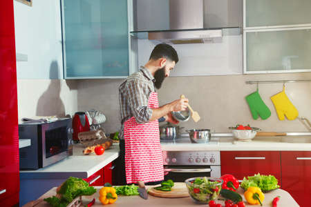 awesome bearded man cooking at kitchen making healthy vegetable saladの写真素材