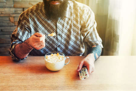 man eating corn flakes with milk and  watching tv with remote controlの写真素材