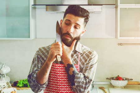 funny man joking at kitchen with knife and beard cutting itの写真素材