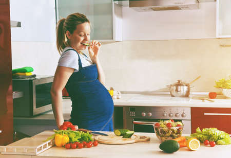 happy pregnant woman on kitchen making healthy salad