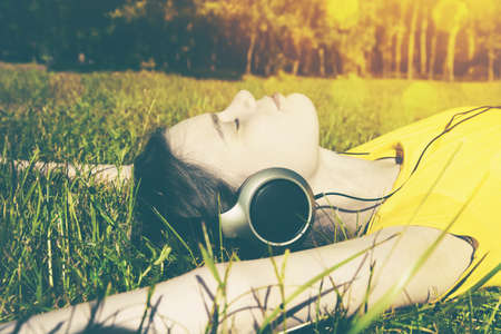 pretty girl lying in summer grass with headphones listening to music and relaxingの写真素材