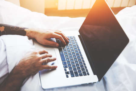 man lying in morning bed with laptop working or studyingの写真素材