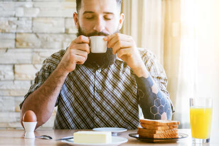 bearded man with breakfast and cup of morning coffeeの写真素材