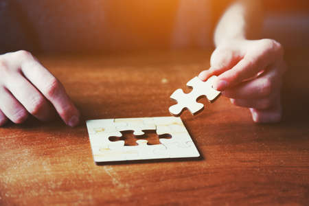 hands solving jigsaw puzzle with wooden piecesの写真素材