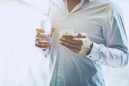 businessman hand holding bottle of water and reading smartphoneの写真素材