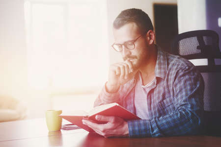 man reading book with cup of tea or coffee at home in morning sunlight