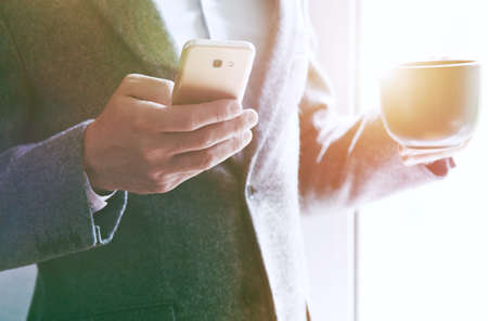 businessman hand holding morning tea or coffee and reading smart phone