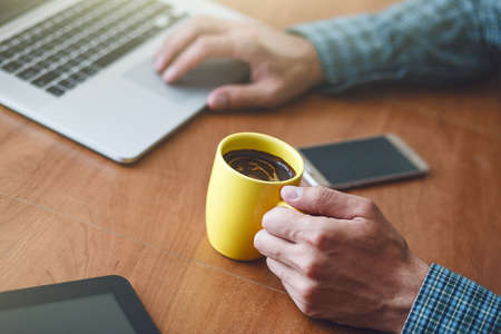man drinking cup of morning coffee at table with laptopの写真素材
