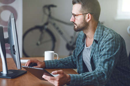 concentrated man with digital tablet and computer at tableの写真素材